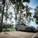 Camping with campervan in Bali featuring van parked near scenic forest and lake, cozy outdoor setup with camp chairs, sunrise backdrop, and peaceful nature surroundings — ideal for road trip adventures and flexible camping stays.