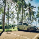 CAMPERVAN - EN - Home 24 East Bali Campervan di tepi pantai saat sunset dengan pasangan duduk santai di depan mobil