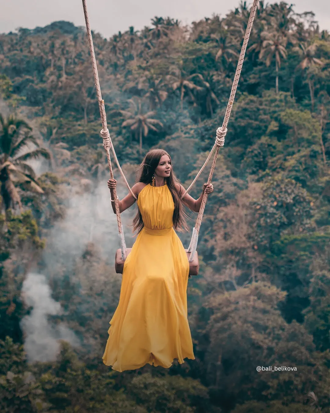 Mujer con vestido amarillo disfrutando del columpio de Bali con el paisaje escénico del bosque de Ubud como fondo..