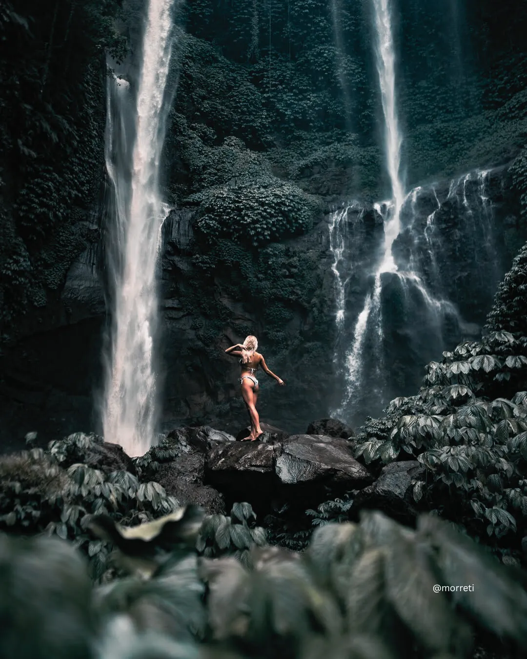 Mujer de pie junto a una pintoresca cascada rodeada por la exuberante jungla del norte de Bali.