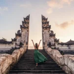 Woman in a long green dress walking up the stone stairs toward the Gate of Heaven at Lempuyang Temple Bali.