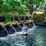 Chorros de agua de piedra y devotos realizando baños rituales en la piscina de purificación de Tirta Empul