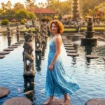 Tourist in flowy dress feeding koi fish at Tirta Gangga Water Palace Bali